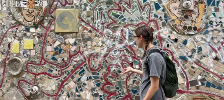 A students stands in front of a mosaic in Philadelphia.